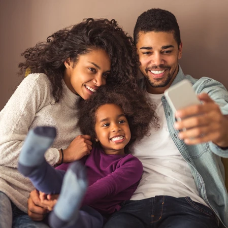 A family of three smiling while taking a selfie, displaying pearly white smiles