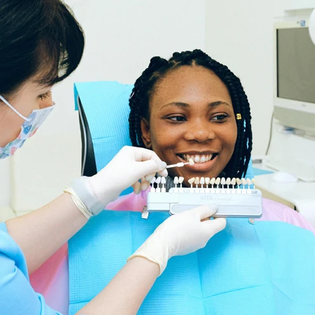 A patient sitting in a dental exam chair while a hygienist color matches their teeth to the best whitening level